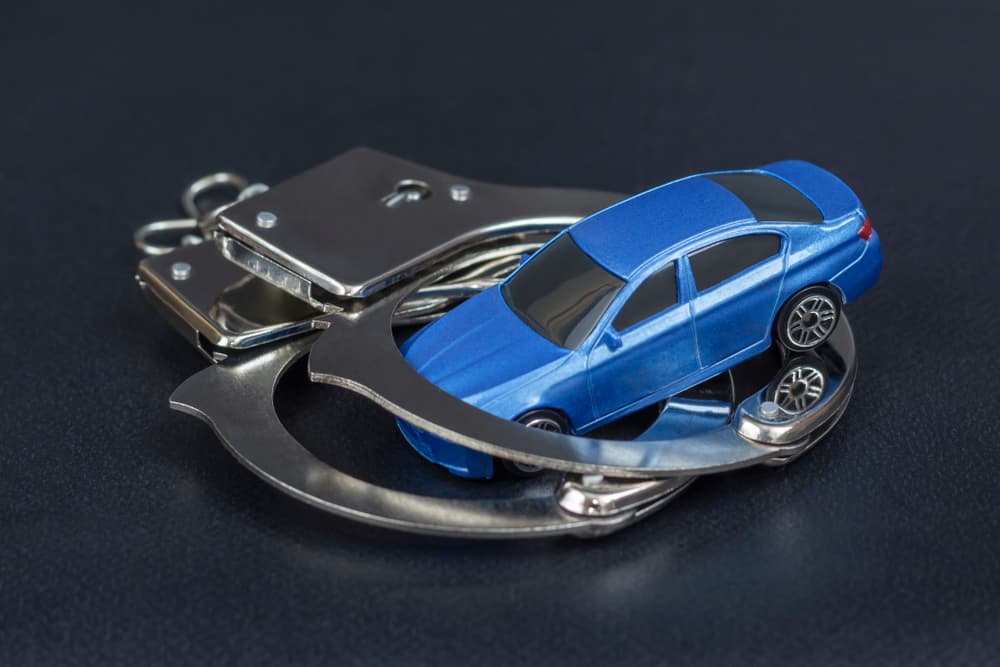 Handcuffs placed on a blue car, symbolizing the concept of car under arrest due to non-payment of debt or car loan, with a black background.