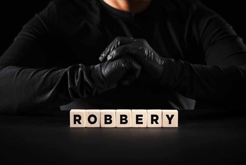 The word robbery written on wooden blocks with a thief with black gloves background