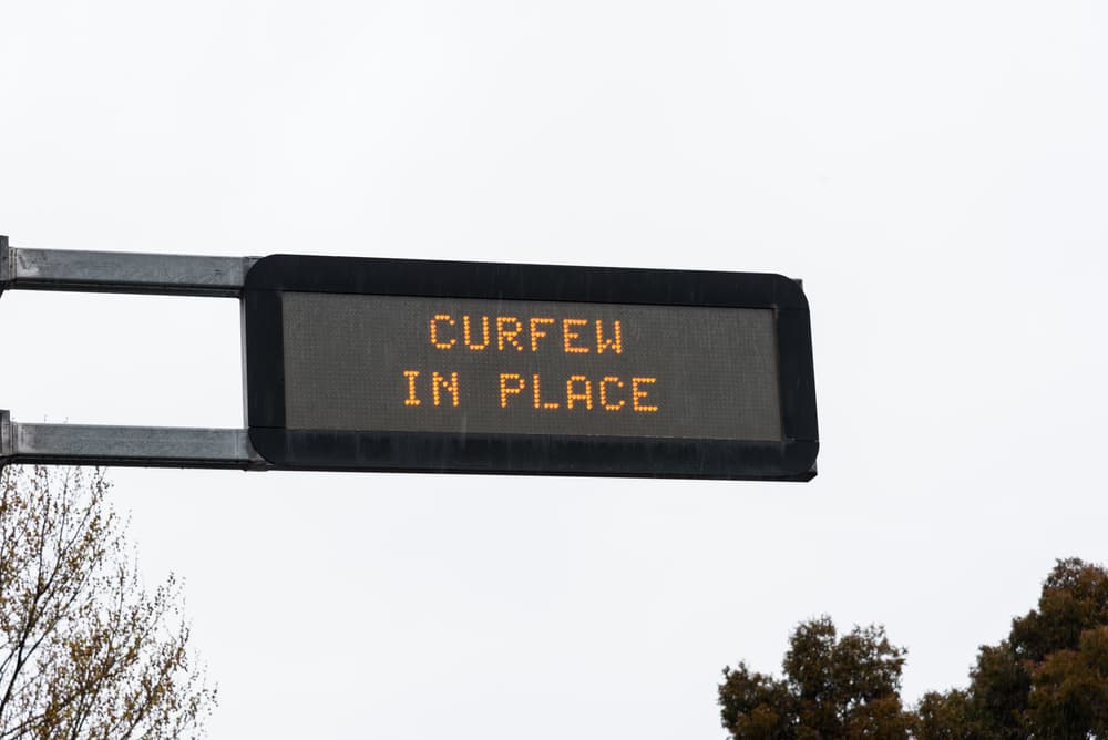 An overhead street sign showing the information about the curfew in place in the city